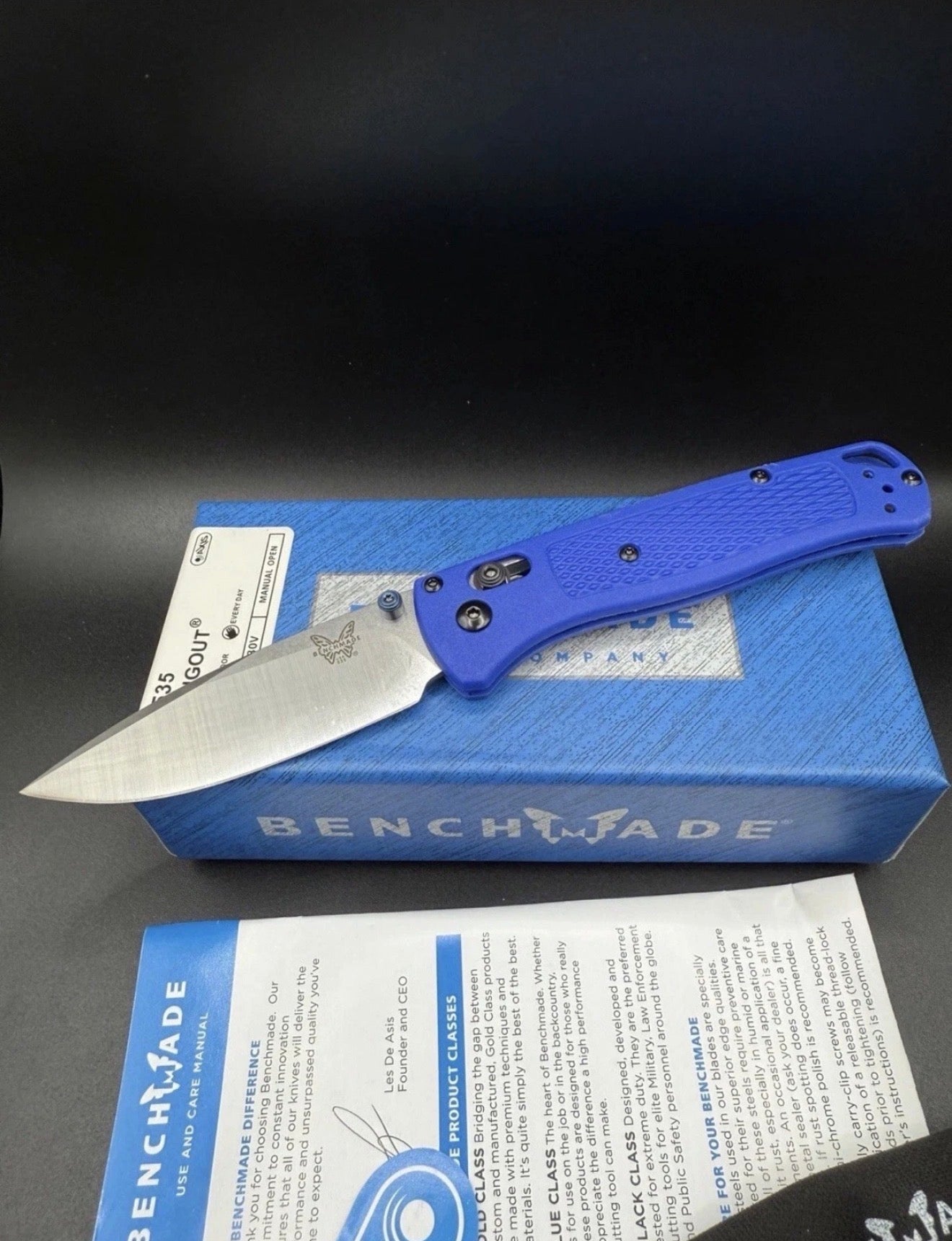 Blue Benchmade knife on a black surface with a blue box and paper in the background.